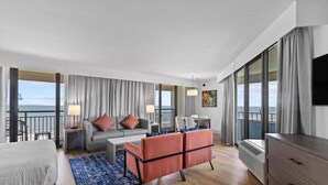 Una habitación de hotel moderna con balcón, un conjunto de sofás, una mesa de comedor y televisión.