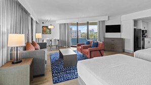 Una habitación de hotel moderna con una cama grande, dos sofás, una mesa de comedor y una zona de cocina.