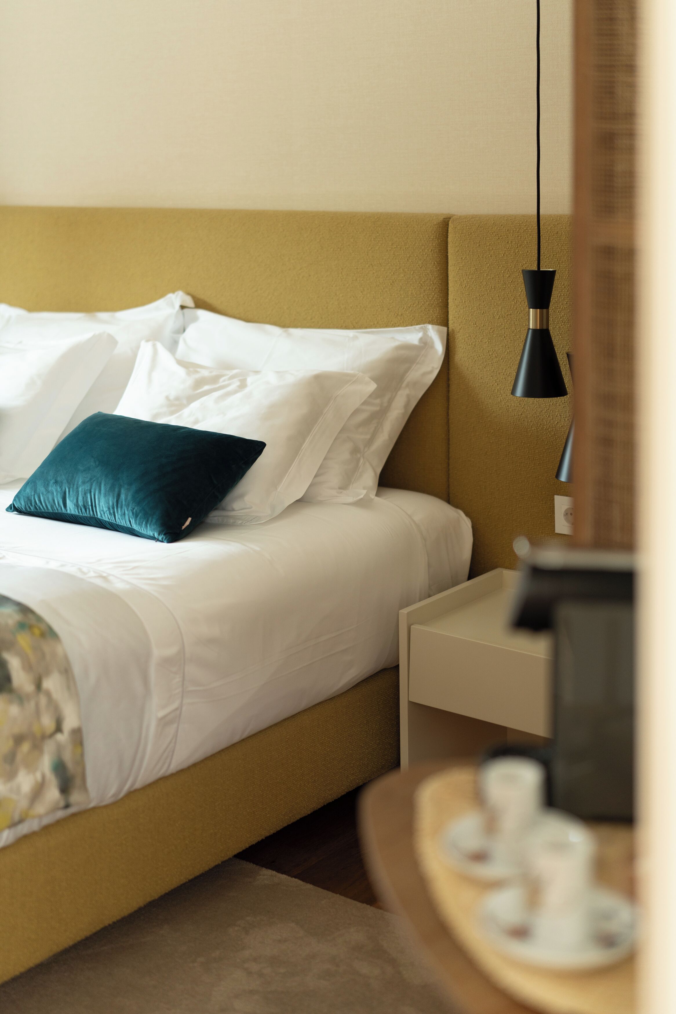 Una cama con sábanas blancas, un almohadón verde, una mesita de noche y una lámpara.