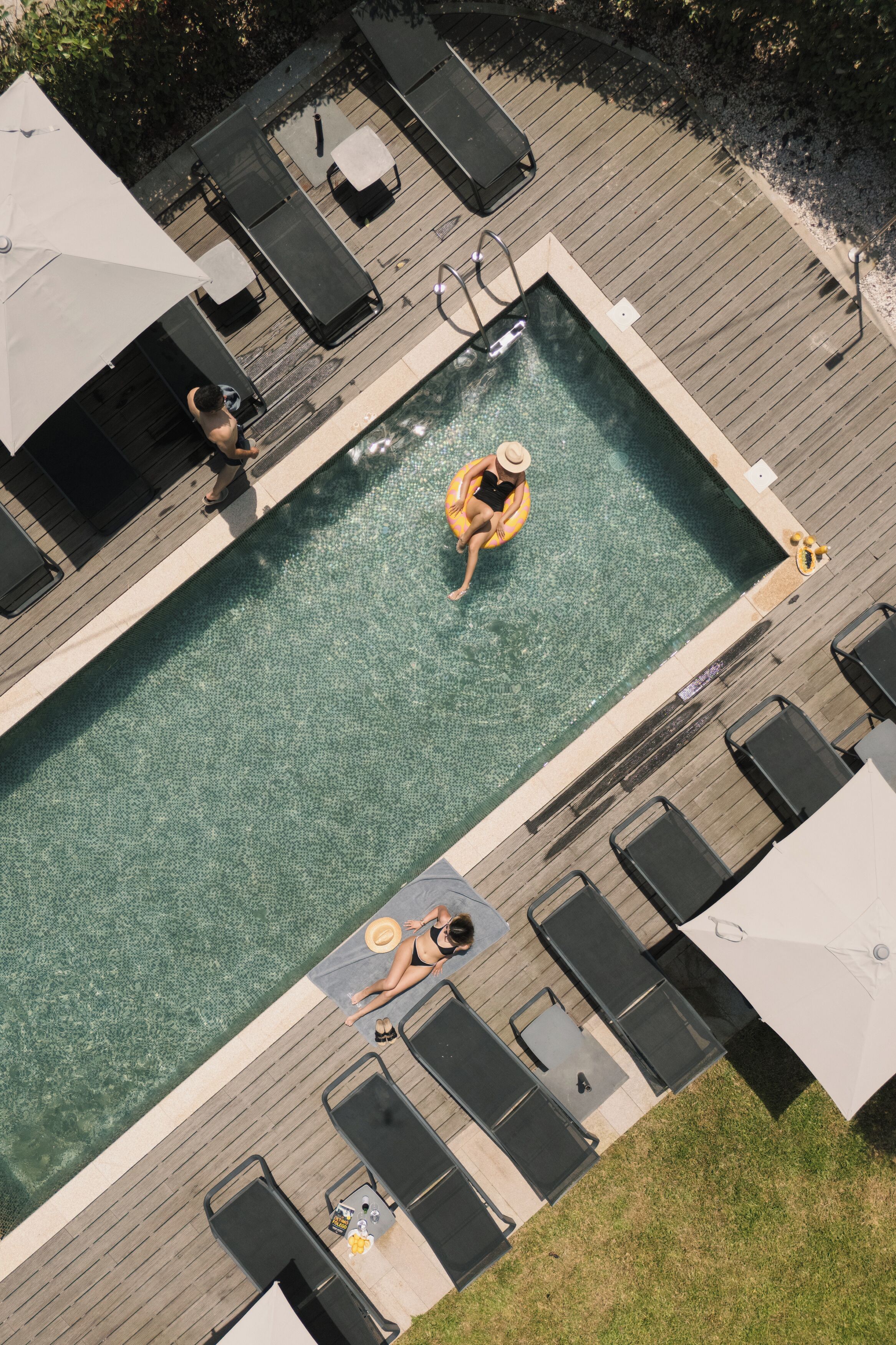 En vy från ovan av en swimmingpool med solstolar och parasoller, omgiven av ett trädäck.