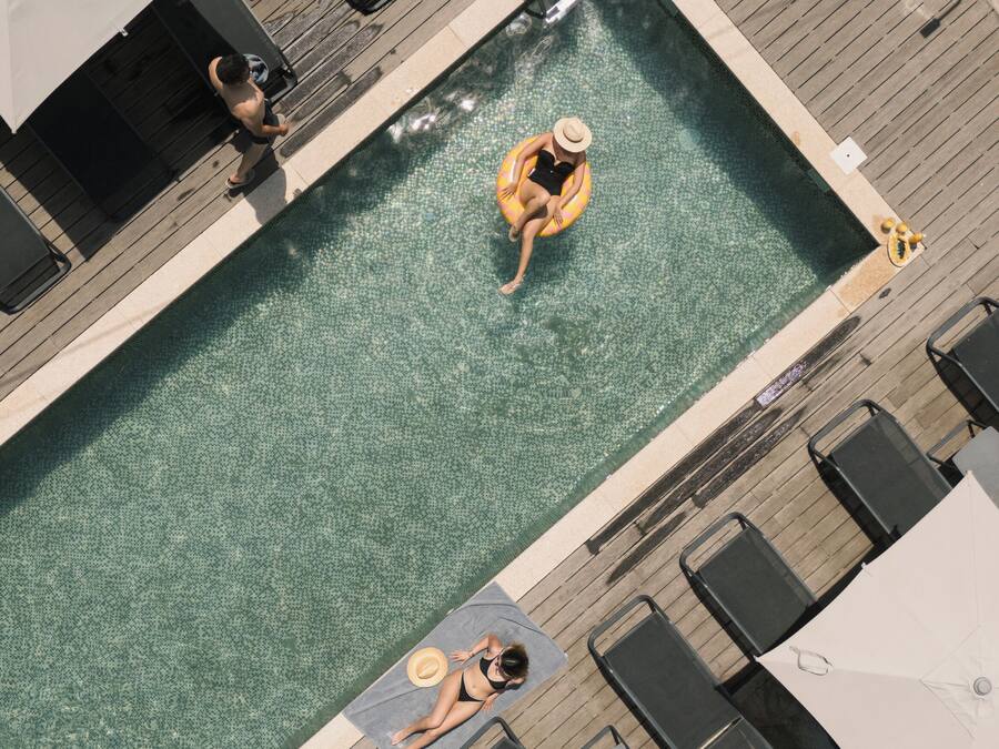 En vy från ovan av en swimmingpool med solstolar och parasoller, omgiven av ett trädäck.