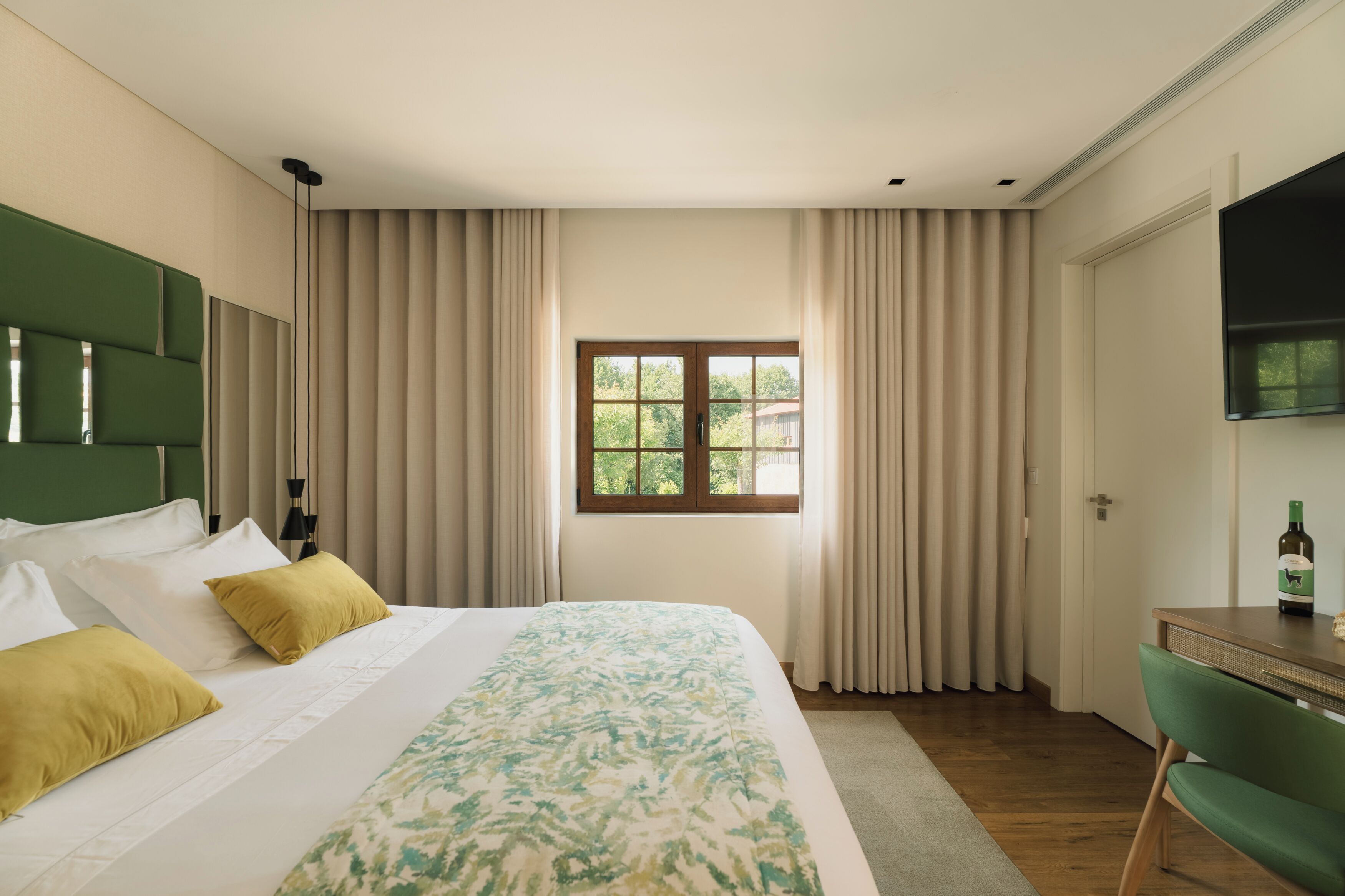 Ein Hotelzimmer mit Bett, Vorhängen, einem Fenster, einem Schreibtisch und einem Stuhl.