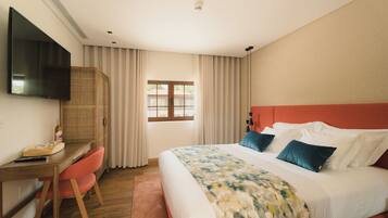 Una habitación de hotel con cama, escritorio con silla, televisor y ventana con cortinas.