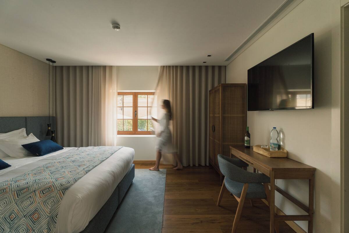 A hotel room with a bed, a desk, a chair, a television, and a wardrobe.