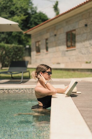 A person reading by a poolside, with a house and greenery in the background. - Constance Retreat - Douro Verde by FERO (Marco de Canaveses)