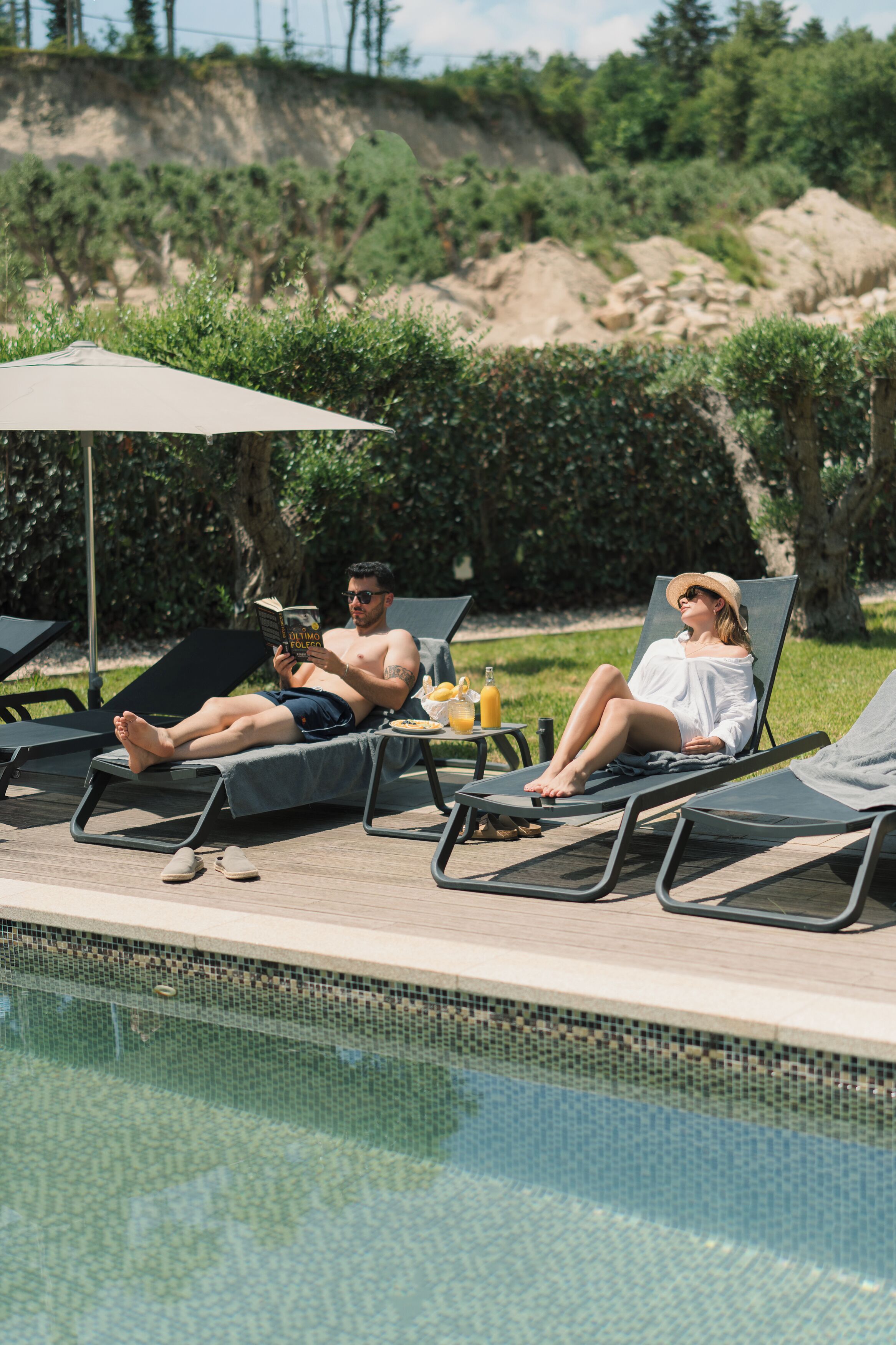A poolside area with lounge chairs, a table with drinks, and a book.