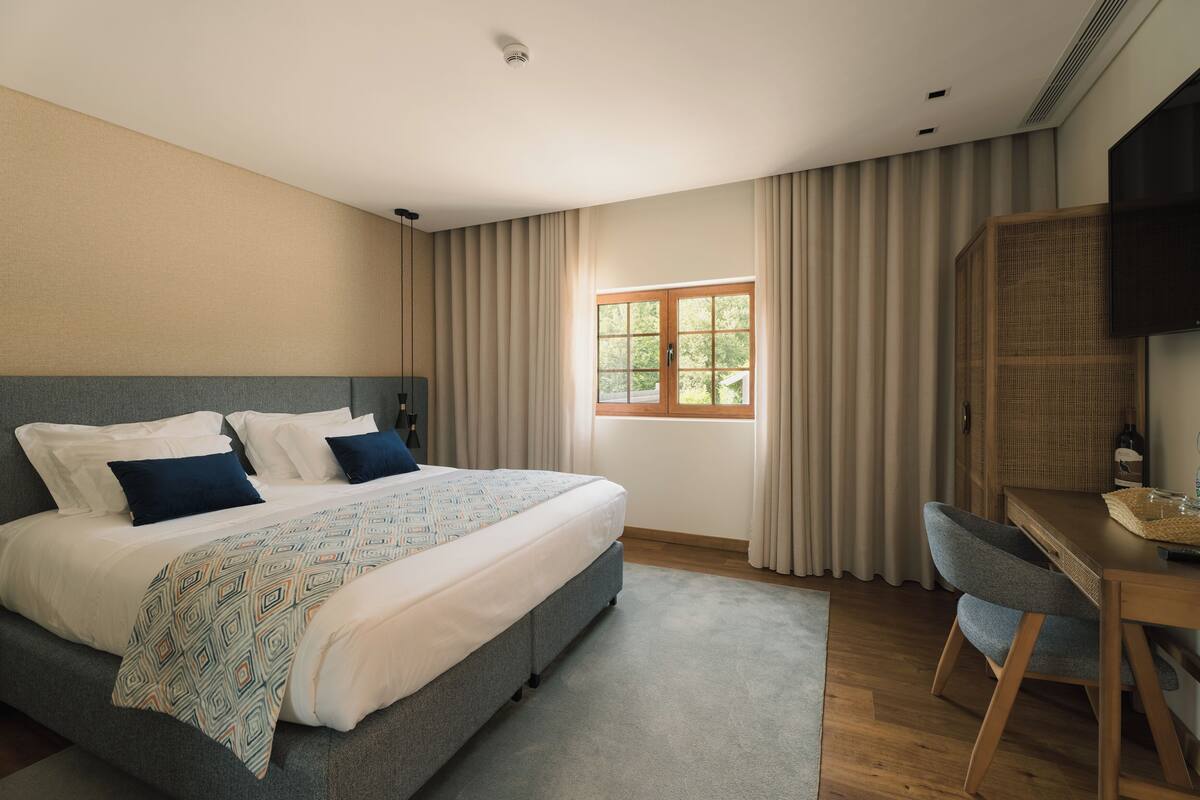A modern bedroom with a large bed, a desk, and a window with curtains.