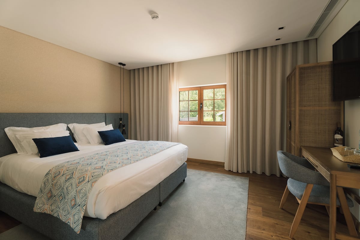 Quarto moderno com uma cama grande, escrivaninha e janela com cortinas.