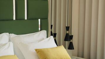 A hotel room with a green headboard, white and yellow pillows, a bed with a patterned bedspread, and black pendant lights.