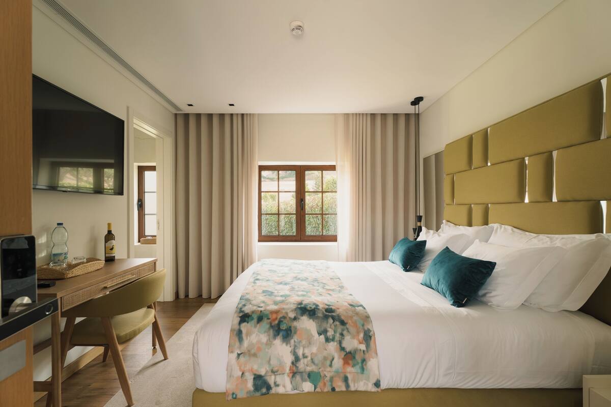 A hotel room with a bed, a desk, a television, and a window with curtains.