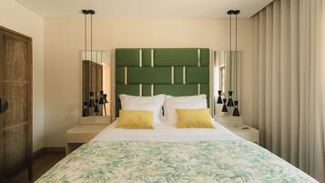 Habitación de hotel con una cama grande, cabecera verde, dos mesitas de noche y un ventanal con cortinas.