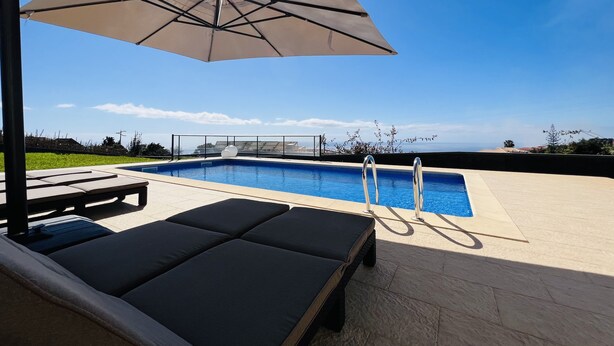 En pool med liggestole og en parasol, omgivet af fliseterrasse og udsigt over landskabet.