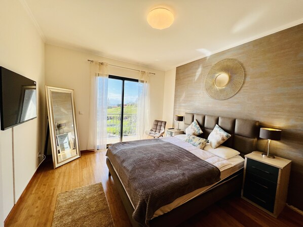 A bedroom with a large bed, a flat-screen TV, a bedside table with a lamp, and a view of a balcony. - Villa Carpe Diem by Your Madeira Rentals (Estreito da Calheta)