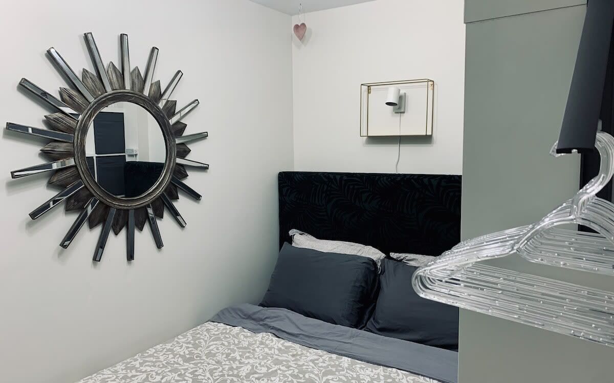 A bedroom with a bed, a wall-mounted mirror, a heart-shaped decoration, and a light fixture.