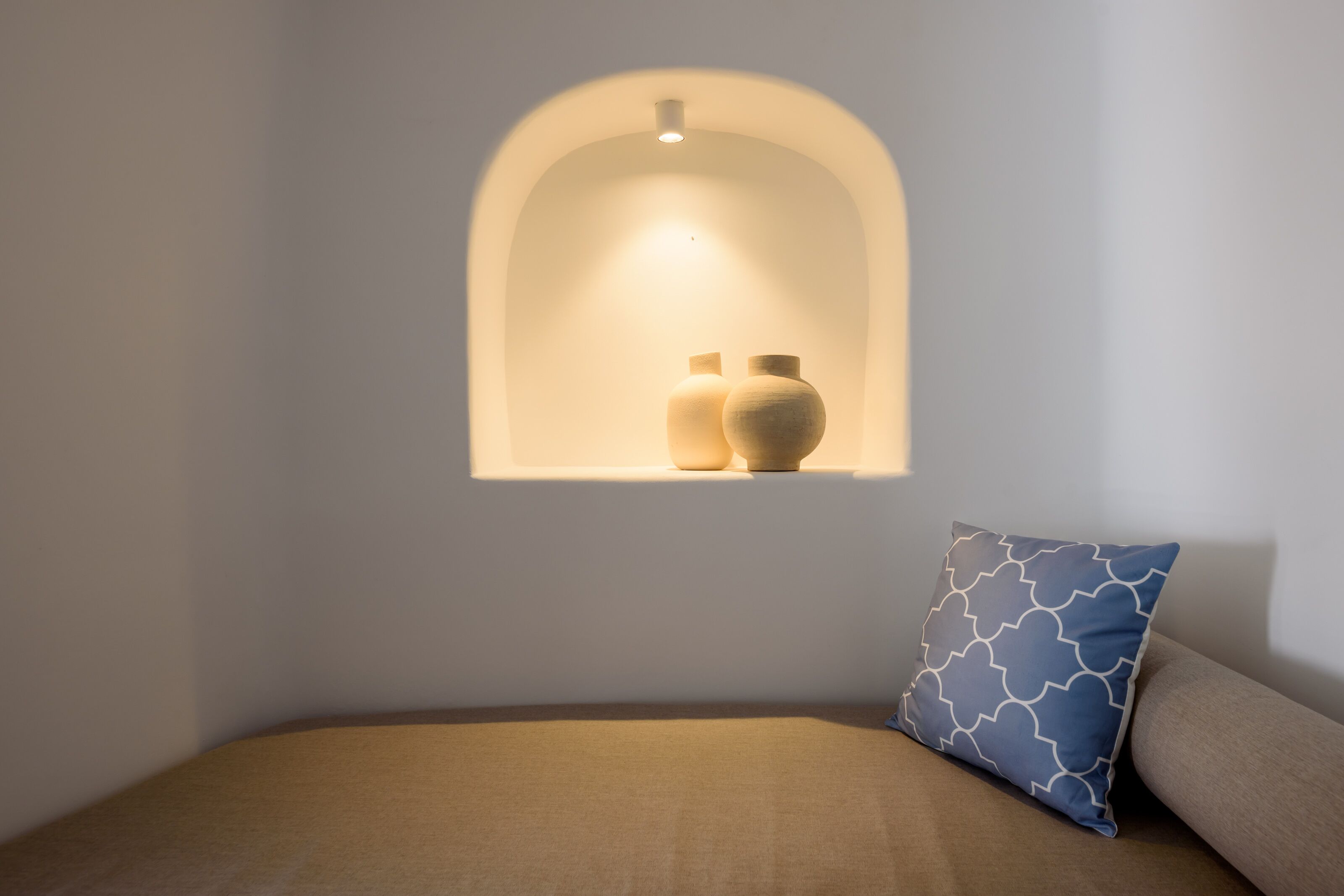 A bedroom with a bed, a wall-mounted shelf with two vases, and a patterned pillow.