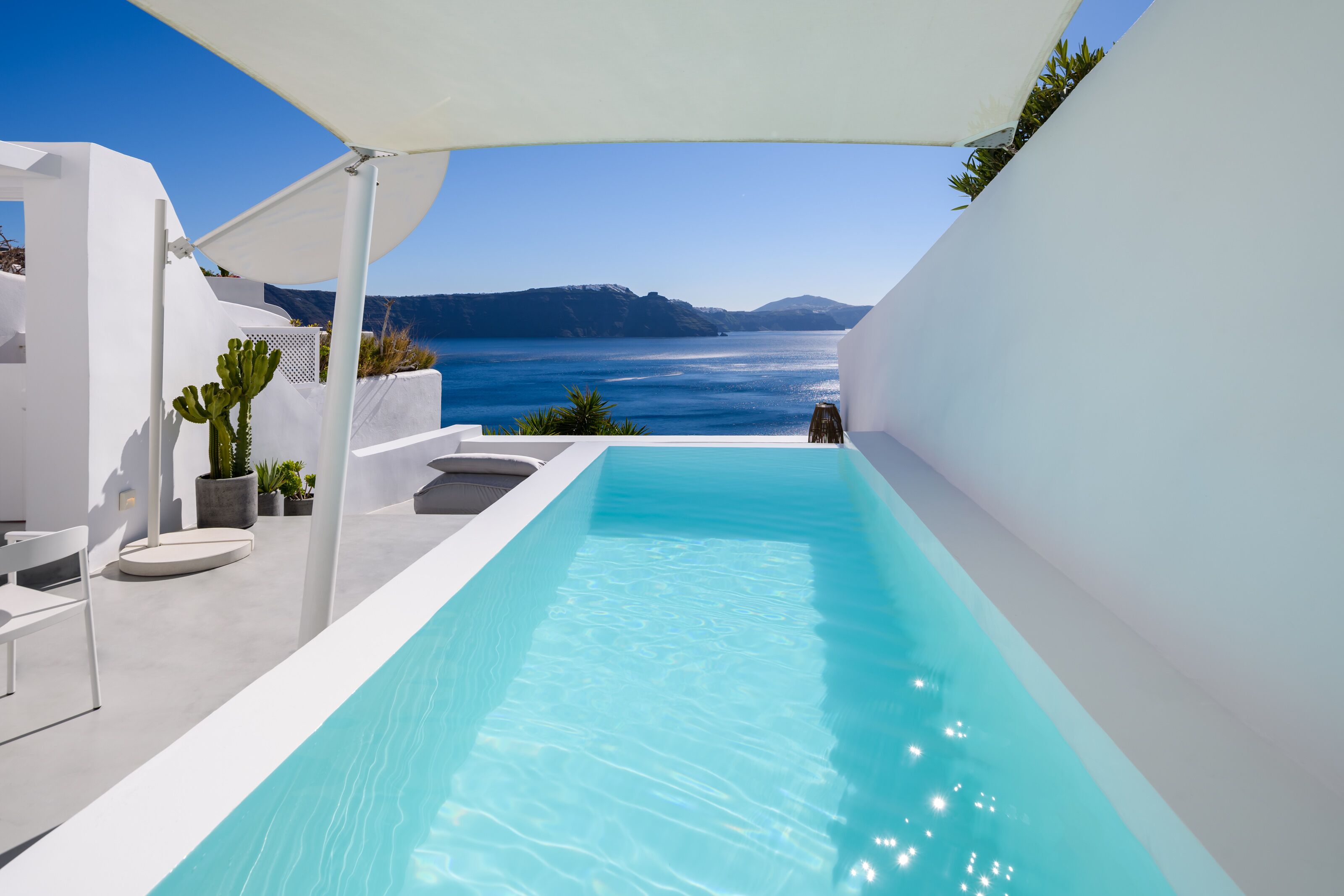 A modern outdoor pool with a clear view of the sea and mountains in the background.