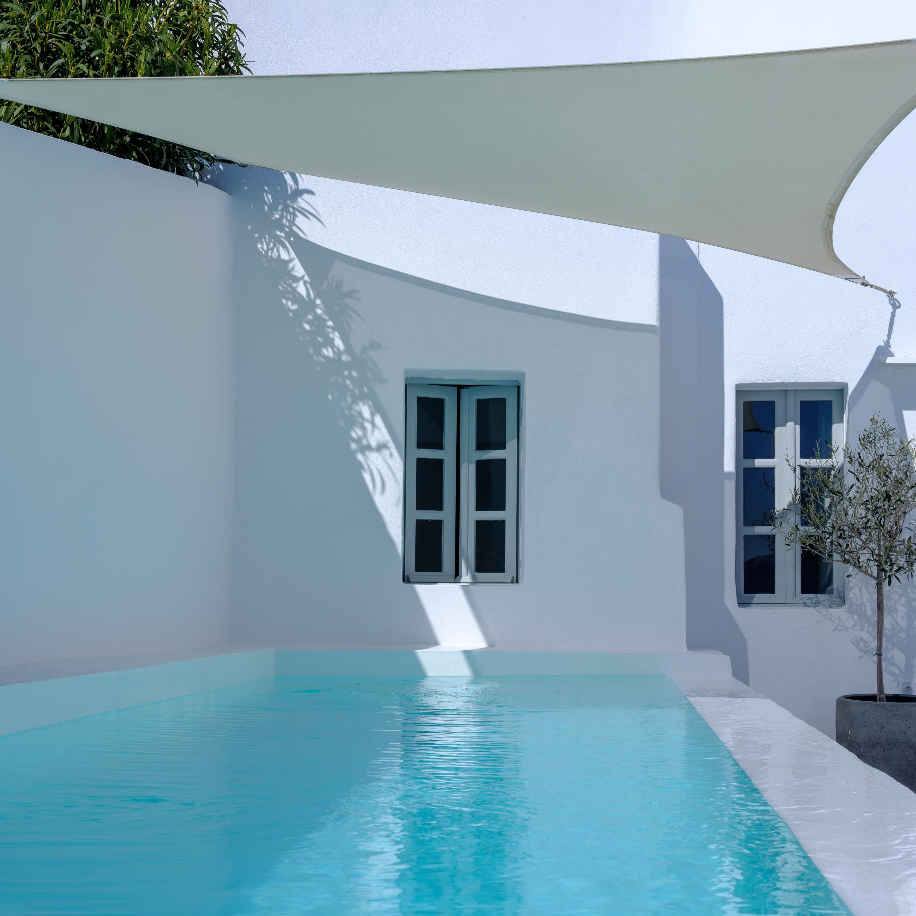 Un área de piscina moderna con piscina azul cristalina, paredes blancas y un ventanal grande.