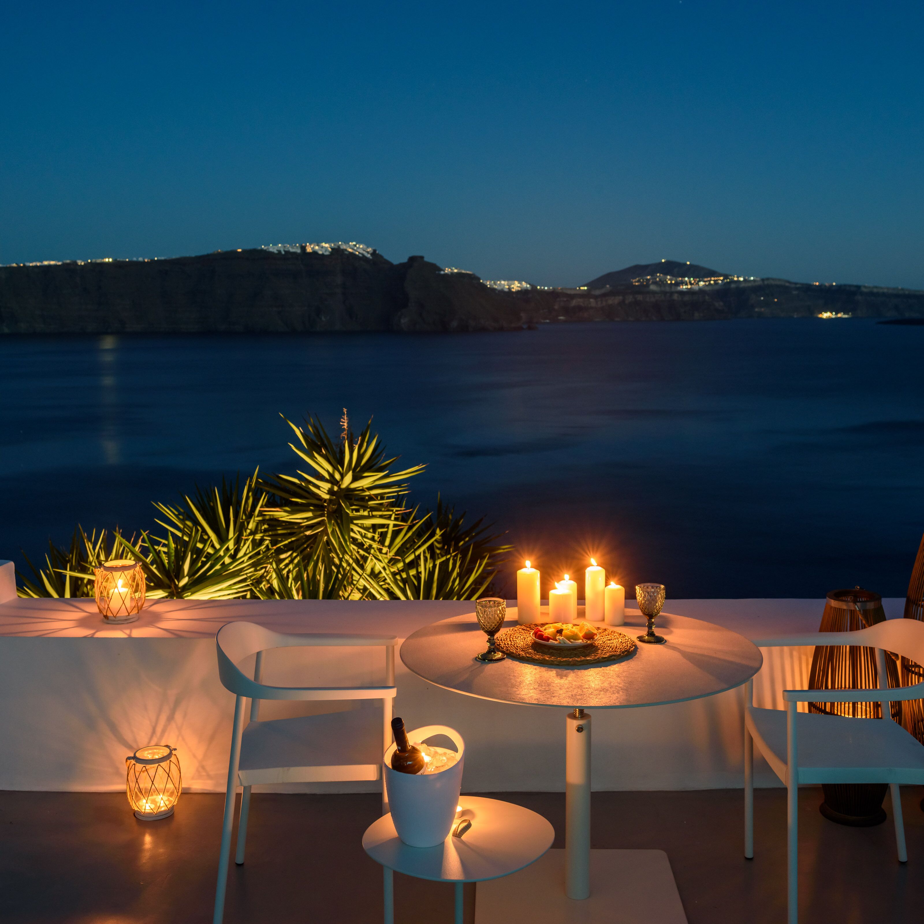 Un espacio de comedor al aire libre con una mesa para dos personas, velas y una botella de vino.