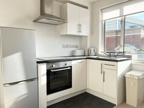 A modern kitchen with white cabinetry, a built-in oven, a stainless steel range hood, and a window providing natural light.