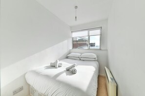 A bedroom with a large window, a bed with white linens, and a radiator.
