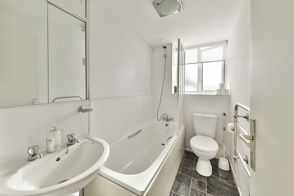 A modern bathroom with a bathtub, sink, toilet, and a window providing natural light.