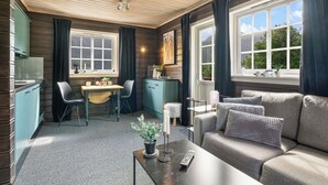 Una habitación acogedora con techo de madera, un rincón de comedor con mesa y sillas, un sofá con cojines y una ventana con cortinas.