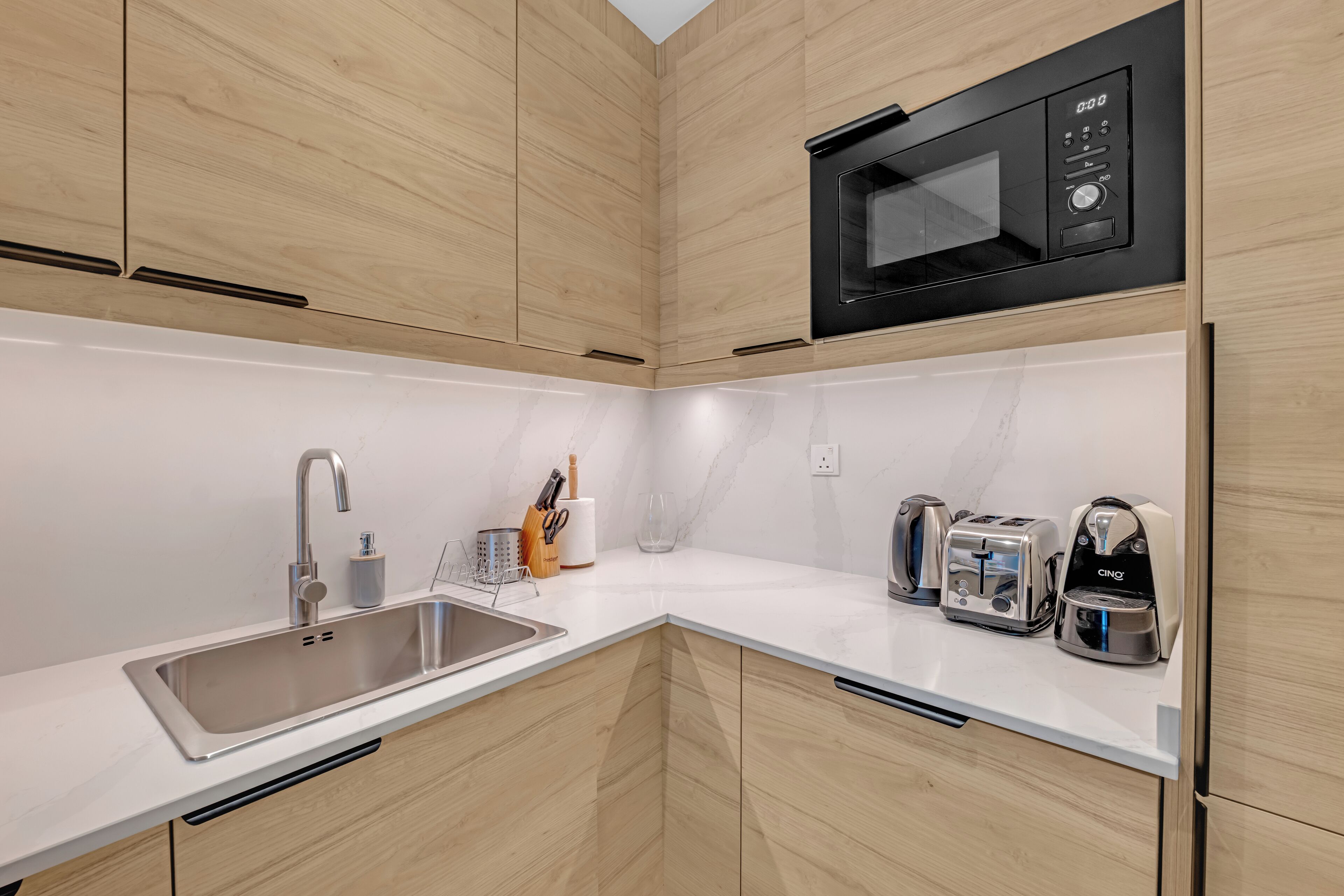 Una cocina moderna con armarios de madera, un lavamanos de acero inoxidable, un microondas y un tostador.