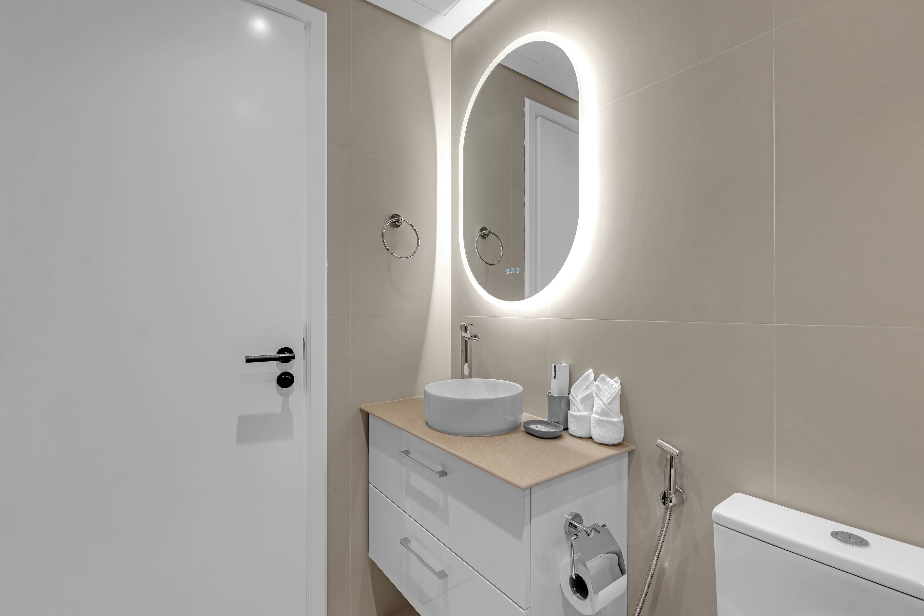 Ein modernes Badezimmer mit rundem Spiegel, Waschbecken, Toilette und Handtuchhalter.