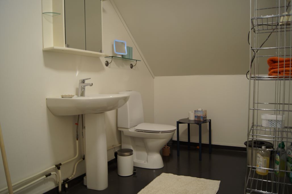 A small bathroom with a sink, toilet, and a small table with toiletries.