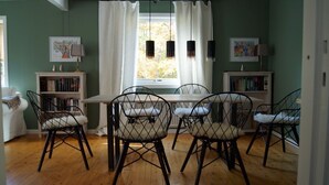 Un coin repas avec une table en bois et quatre chaises, deux étagères et une fenêtre avec des rideaux.