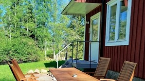 Une table et des chaises en bois sont disposées sur une terrasse, offrant une vue sur un bâtiment rouge et sur la verdure.
