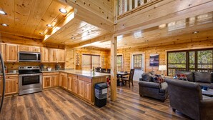 A spacious kitchen with wooden cabinets, a central island, stainless steel appliances, and a dining area with a leather sofa. - 5BR Cabin Near Parkway | Views, Hot Tub, Theater (Pigeon Forge)