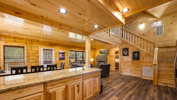 A wooden cabin interior with a kitchen area, dining table, and a staircase leading to an upper level. - 5BR Cabin Near Parkway | Views, Hot Tub, Theater (Pigeon Forge)