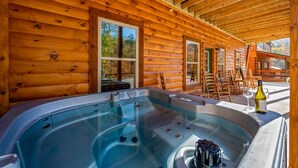 A wooden cabin with a hot tub, outdoor seating, and a bottle of wine. - 5BR Cabin Near Parkway | Views, Hot Tub, Theater (Pigeon Forge)