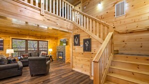 A wooden cabin interior with a staircase, a fireplace, and a living area with sofas and a lamp. - 5BR Cabin Near Parkway | Views, Hot Tub, Theater (Pigeon Forge)