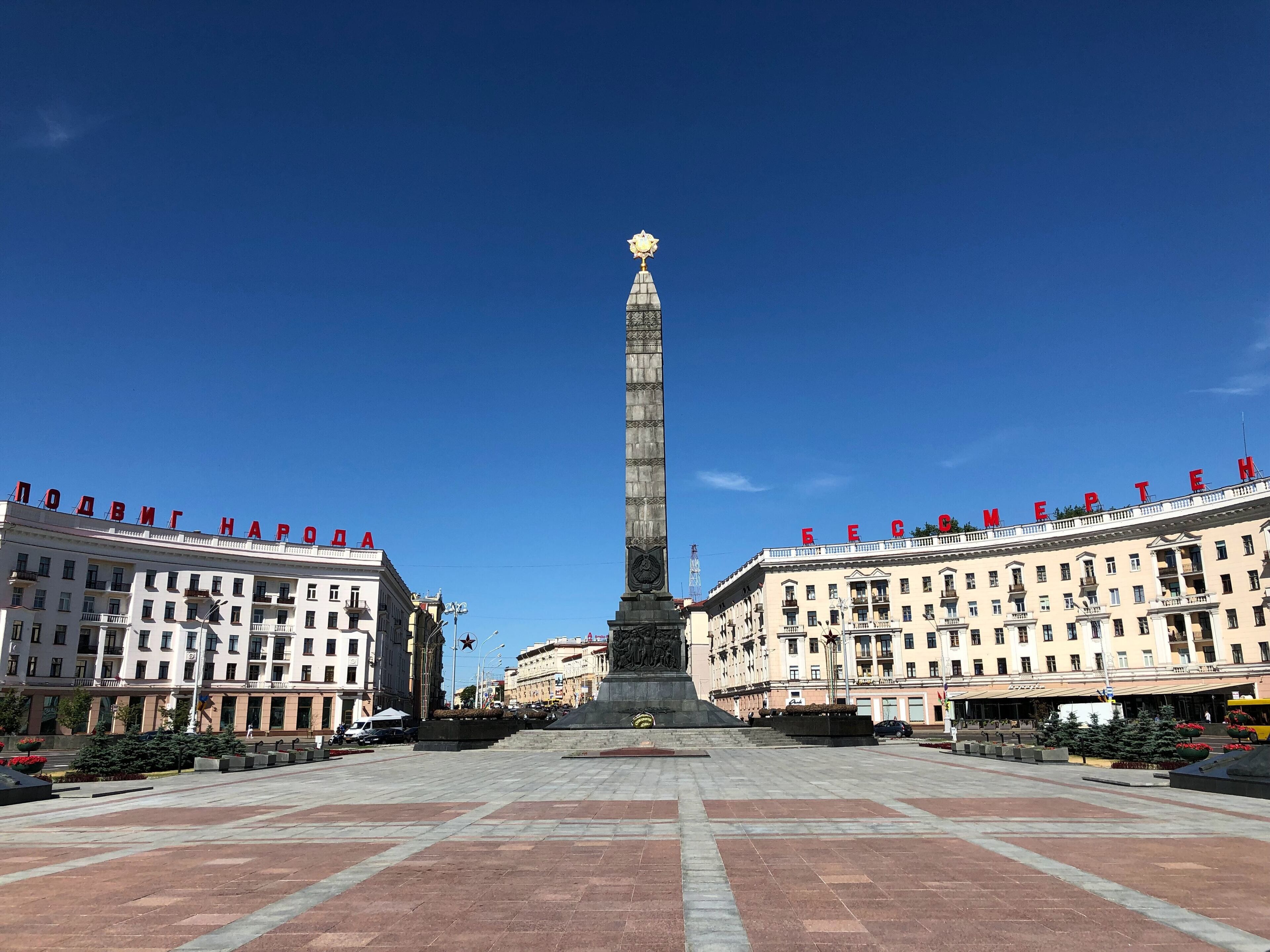 A monument with a star on top, flanked by two large buildings with red letters on top.