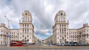 A street view with a red double-decker bus, historic buildings with towers, and a clear sky.