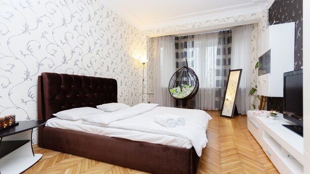 A bedroom with a large bed, a hanging chair, a TV, and a bedside table.