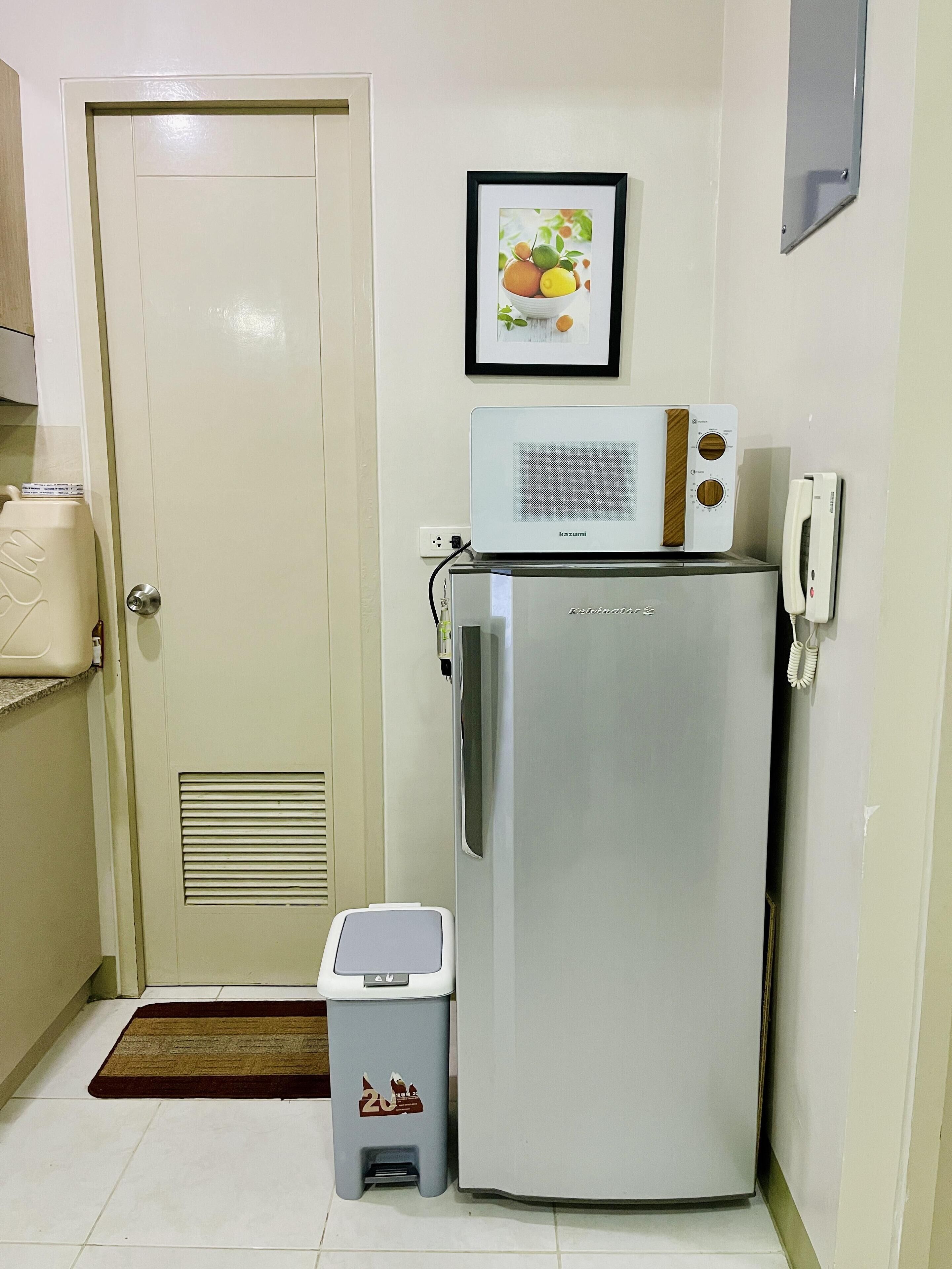 Una cocina compacta con refrigerador, microondas, un cesto de basura y un cuadro en la pared.