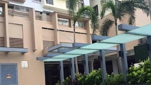 Une piscine avec une terrasse carrelée, entourée d’un espace extérieur couvert agrémenté de palmiers et, au fond, d’un immeuble à plusieurs étages.