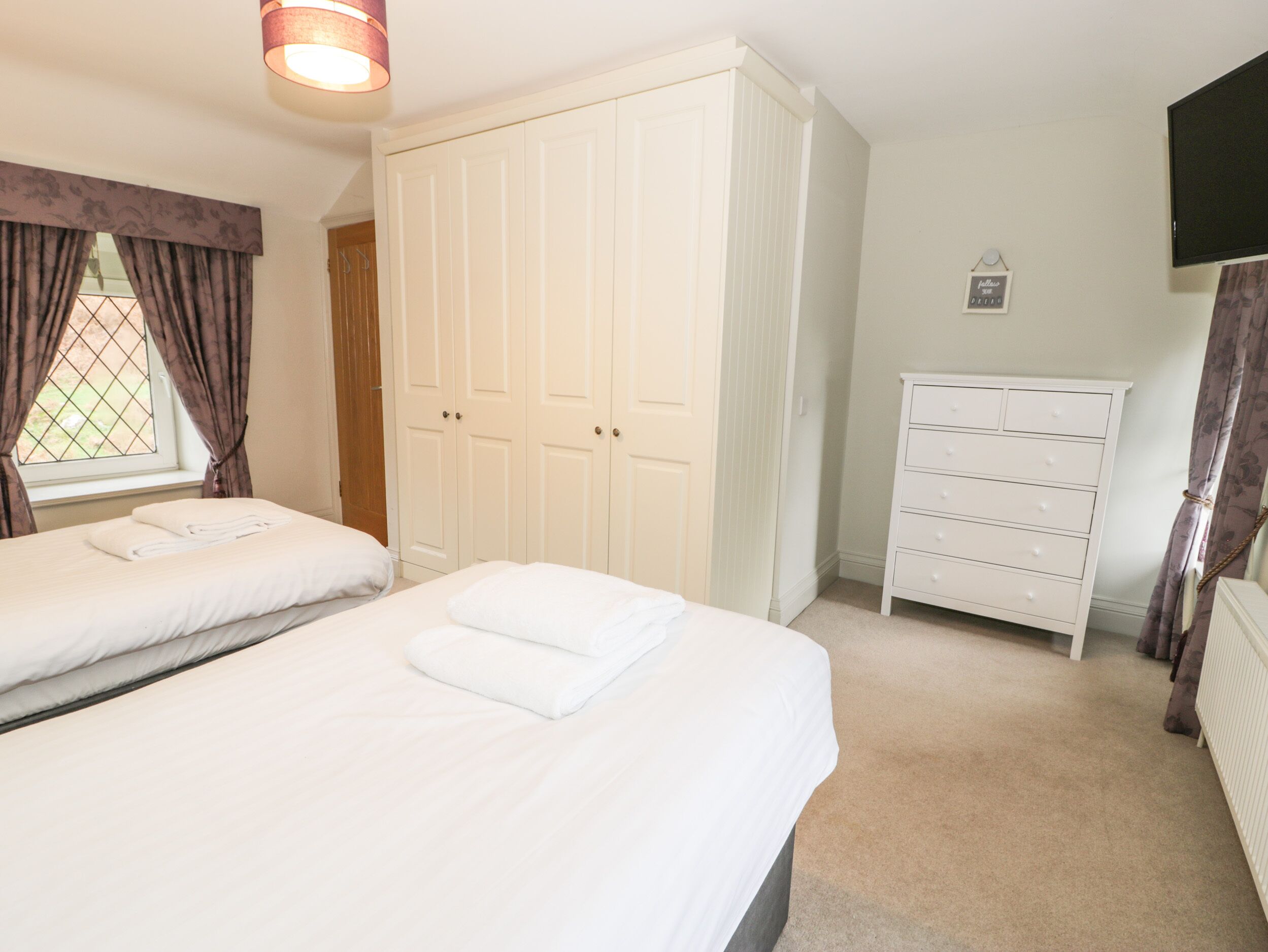 A bedroom with two beds, a wardrobe, a dresser, and a television.