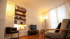 Un salon avec un mur en briques blanches, des étagères en bois, un téléviseur à écran plat, un canapé et une table basse.