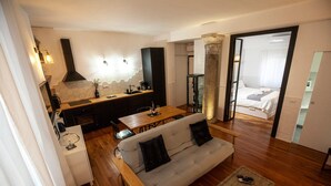 Un salon moderne avec un canapé, une table basse et un coin repas. On y trouve une cuisine équipée d’une cuisinière et d’un réfrigérateur. Un lit est visible au fond.