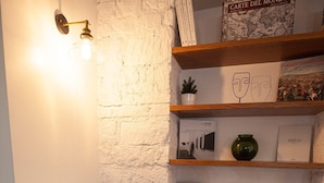 Une pièce d’angle avec un mur en briques blanches, une chaise en bois et une bibliothèque contenant divers livres et objets décoratifs.