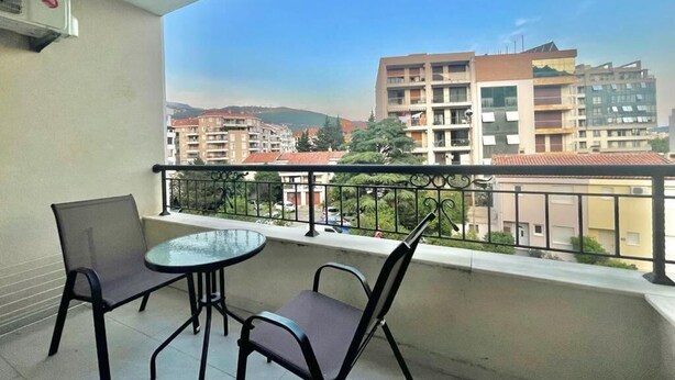 Un balcón con una mesa y dos sillas, con vistas a una zona residencial con edificios y vegetación.