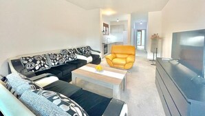 Una sala de estar moderna con un conjunto de sofás, una mesa de centro, un televisor y un sillón naranja.