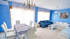 Un salón con pared azul, una zona de comedor con mantel estampado y una araña.
