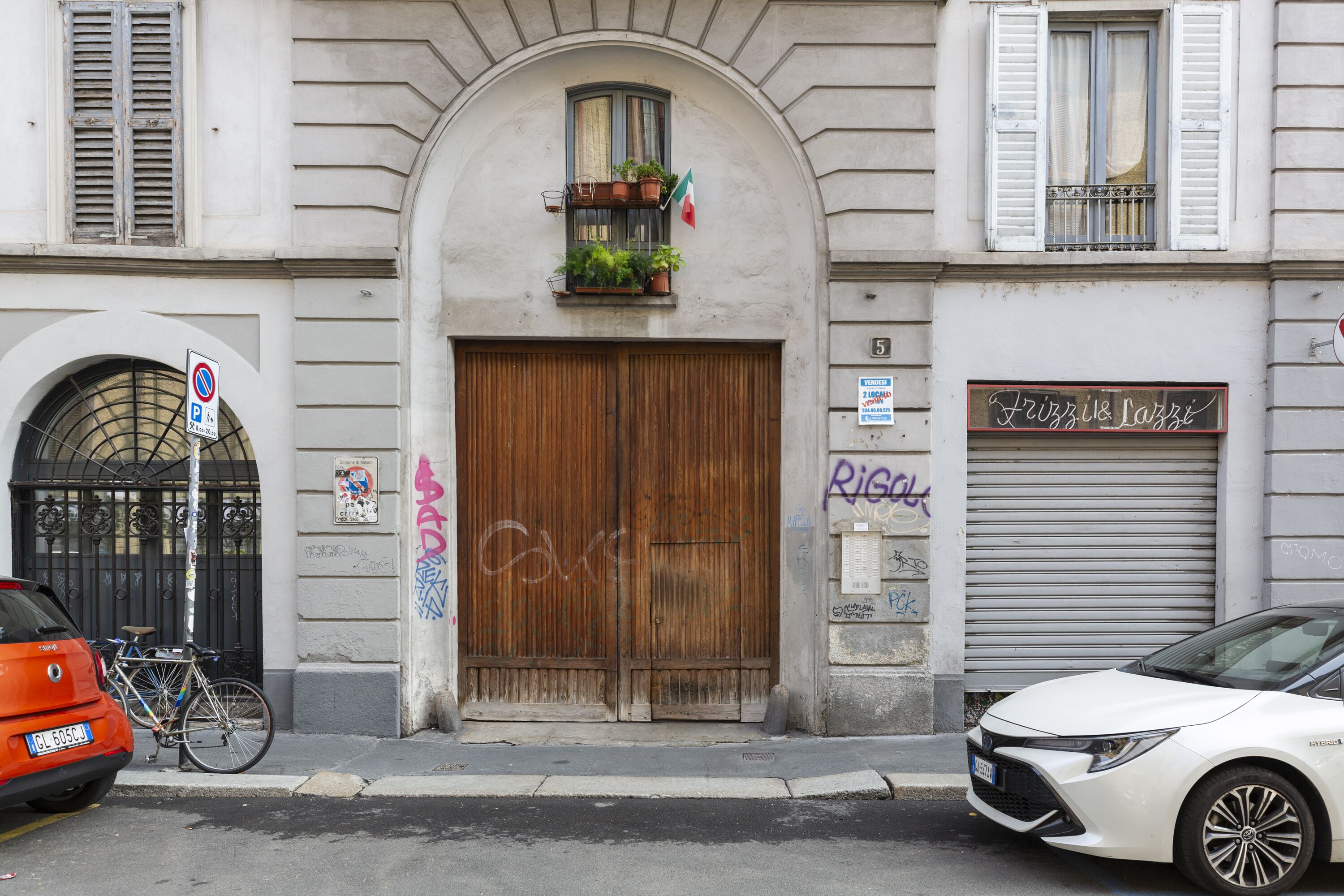 Un bâtiment doté d’une grande porte en bois, d’un balcon orné de plantes et d’une enseigne indiquant « Frizzi & Lazzi ».