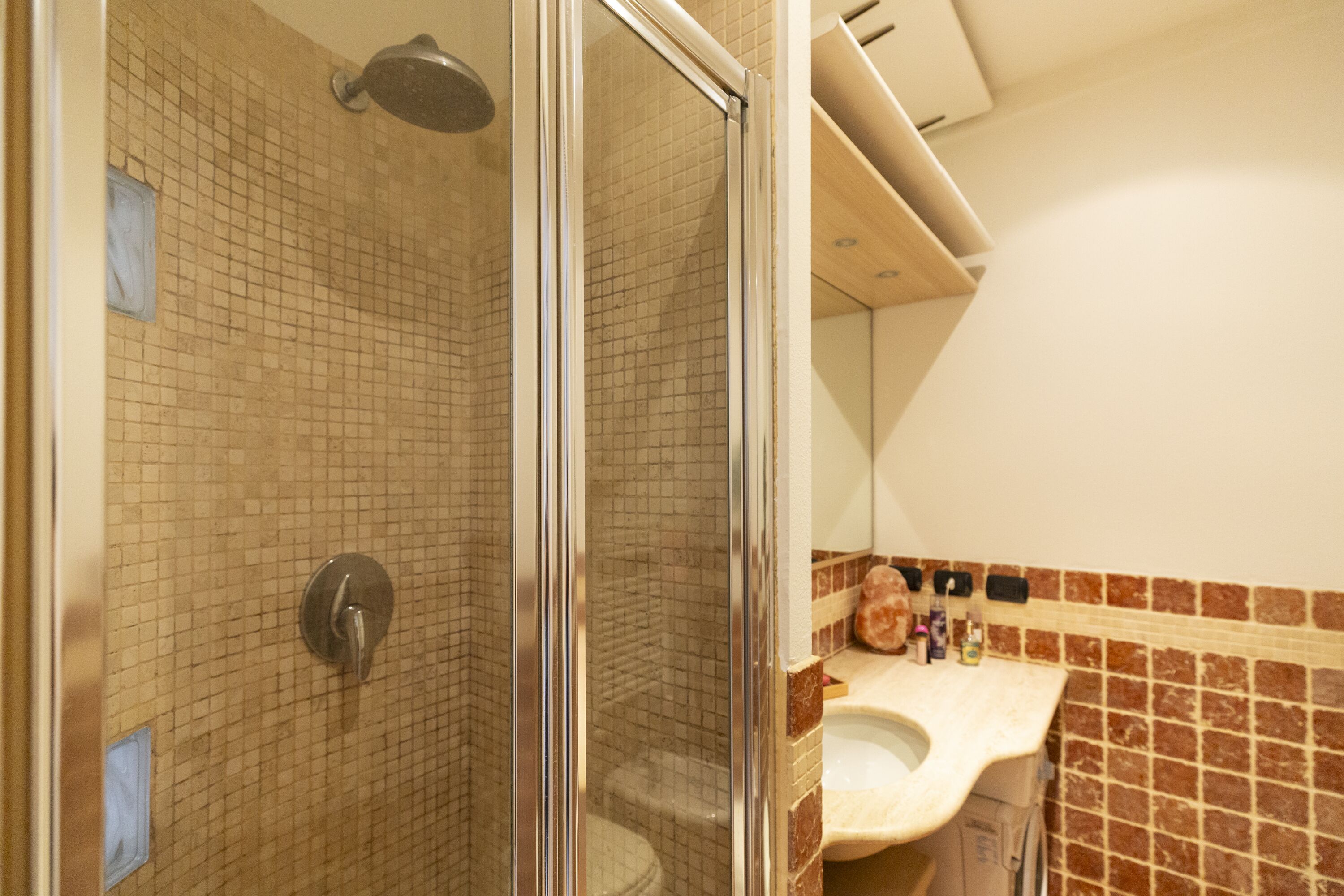 Une salle de bain avec une douche à parois de verre, un mur carrelé et un lavabo équipé de produits de toilette.