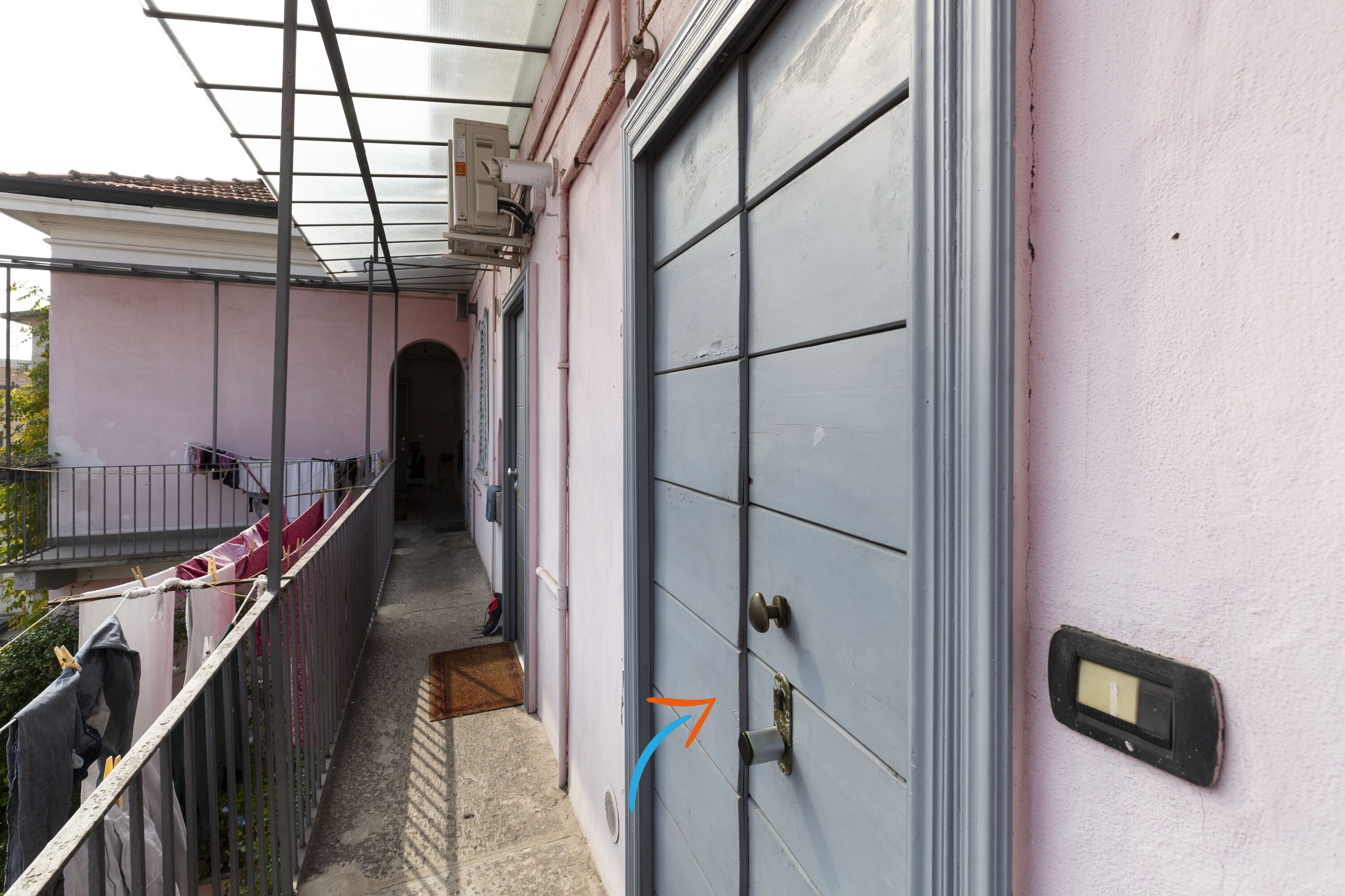A narrow outdoor corridor with a metal fence, a door with a handle, and a small window.